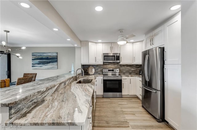 kitchen with appliances with stainless steel finishes, kitchen peninsula, light stone countertops, and white cabinets