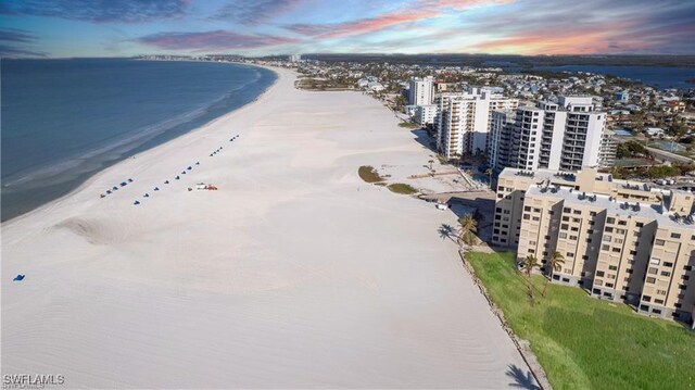 aerial view at dusk featuring a water view and a beach view