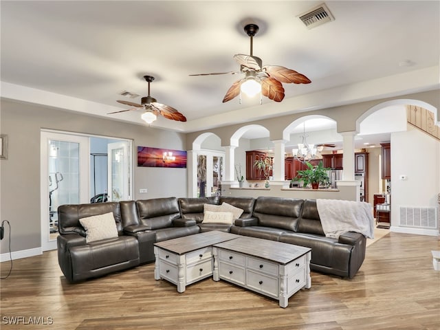 living room featuring ornate columns, light hardwood / wood-style flooring, and ceiling fan with notable chandelier