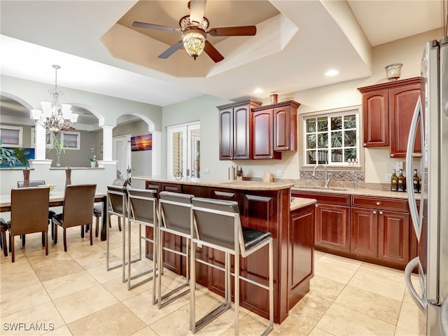 kitchen featuring a center island, ceiling fan with notable chandelier, stainless steel fridge, a tray ceiling, and decorative light fixtures