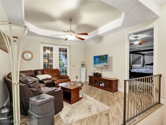 living room with a raised ceiling, french doors, and light wood-type flooring