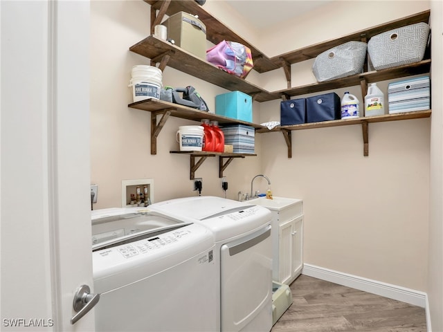 clothes washing area with cabinets, sink, light hardwood / wood-style flooring, and washing machine and clothes dryer