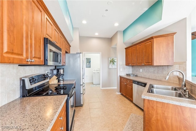 kitchen with appliances with stainless steel finishes, washer / clothes dryer, brown cabinetry, and a sink