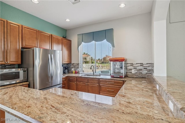 kitchen with sink, tasteful backsplash, light stone counters, kitchen peninsula, and appliances with stainless steel finishes