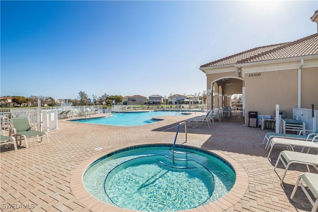 community pool featuring a patio area, a hot tub, and fence