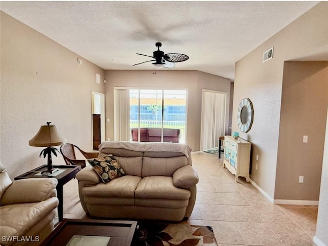 living room featuring a textured ceiling, light tile patterned floors, visible vents, baseboards, and a ceiling fan