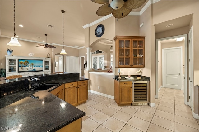 kitchen with pendant lighting, dark stone counters, crown molding, beverage cooler, and decorative columns