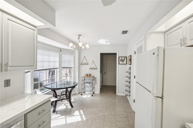 kitchen with light stone countertops, tasteful backsplash, pendant lighting, white refrigerator, and a chandelier