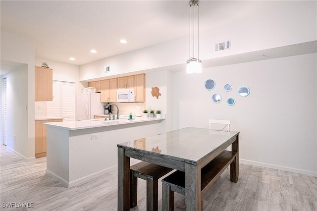 kitchen with kitchen peninsula, white appliances, pendant lighting, light brown cabinets, and light hardwood / wood-style floors