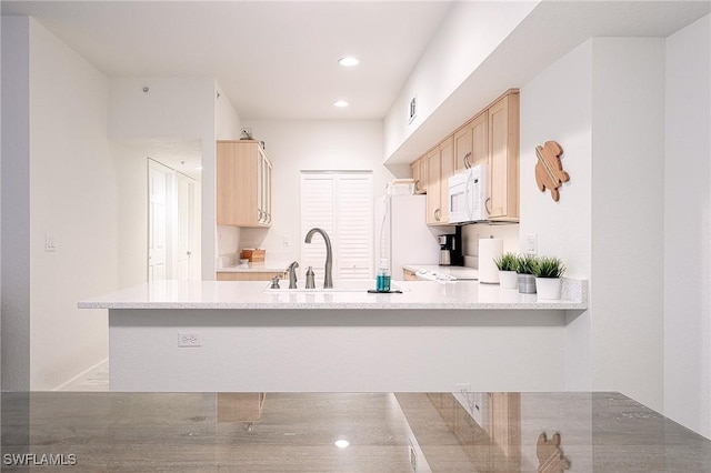 kitchen featuring kitchen peninsula, light brown cabinetry, white appliances, and sink