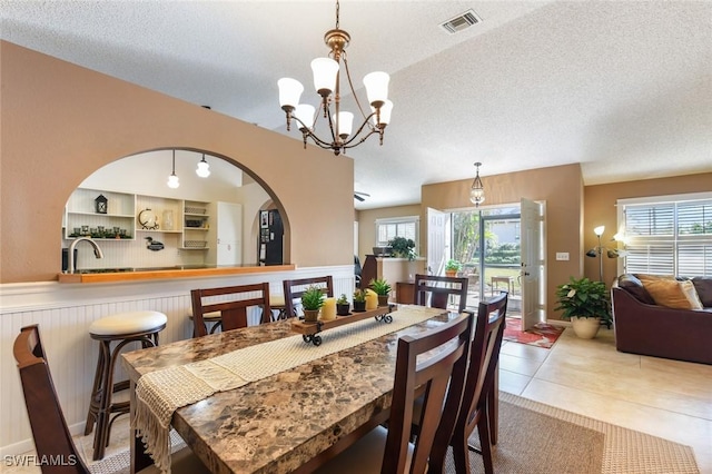 dining room with sink, light tile patterned flooring, a textured ceiling, and an inviting chandelier