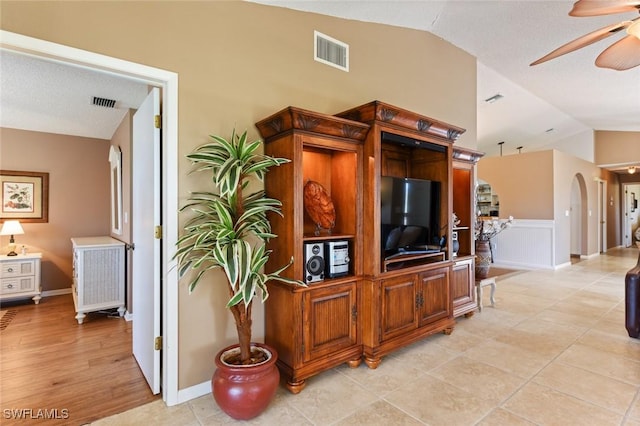 living room with ceiling fan, light hardwood / wood-style floors, lofted ceiling, and a textured ceiling