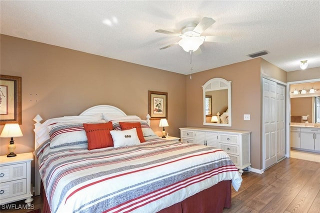 bedroom with ensuite bathroom, a textured ceiling, ceiling fan, wood-type flooring, and a closet