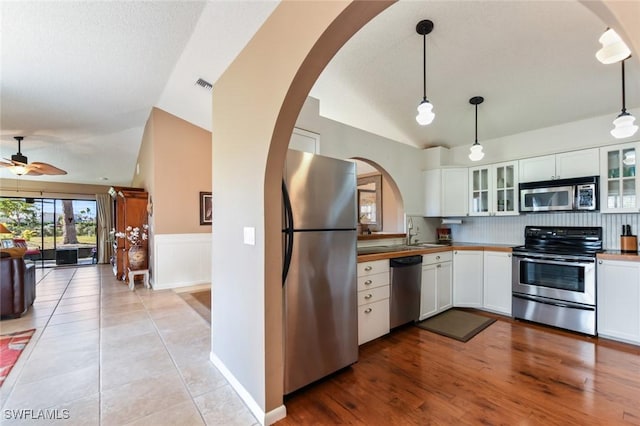 kitchen featuring appliances with stainless steel finishes, vaulted ceiling, light hardwood / wood-style floors, white cabinetry, and hanging light fixtures