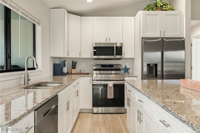 kitchen featuring white cabinets, sink, vaulted ceiling, light stone countertops, and stainless steel appliances