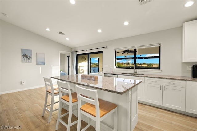 kitchen with light stone countertops, sink, a center island, light hardwood / wood-style flooring, and a kitchen bar