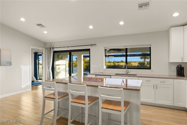 kitchen featuring white cabinetry, sink, light stone countertops, lofted ceiling, and a kitchen island