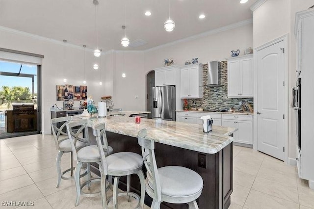 kitchen with wall chimney exhaust hood, a large island with sink, decorative light fixtures, stainless steel fridge with ice dispenser, and white cabinetry