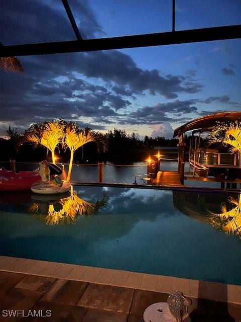 pool at dusk featuring a lanai and a water view