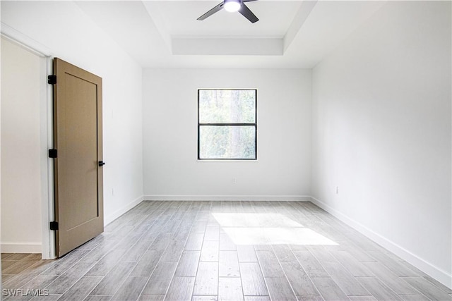 spare room with light hardwood / wood-style flooring, ceiling fan, and a tray ceiling