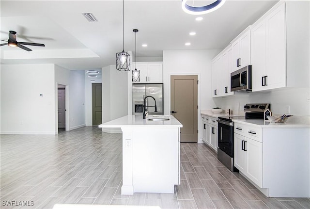 kitchen with pendant lighting, sink, appliances with stainless steel finishes, an island with sink, and white cabinets