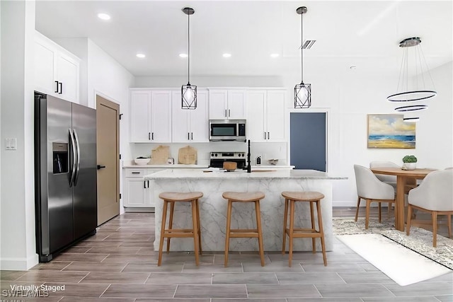 kitchen featuring white cabinetry, hanging light fixtures, stainless steel appliances, and a center island with sink