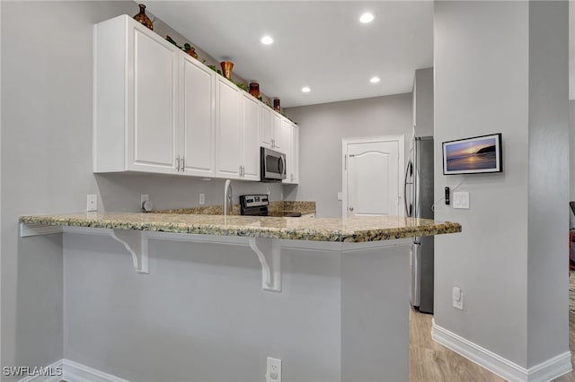 kitchen featuring light hardwood / wood-style flooring, kitchen peninsula, a kitchen bar, white cabinets, and appliances with stainless steel finishes