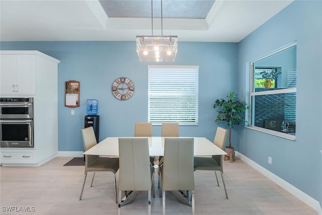 dining space featuring light wood-type flooring, a tray ceiling, and a wealth of natural light