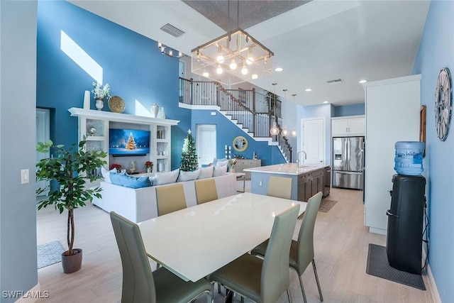 dining area featuring sink, light hardwood / wood-style flooring, a towering ceiling, and an inviting chandelier