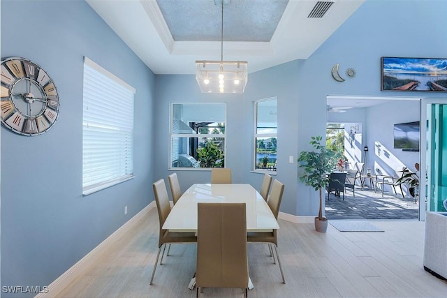 dining space with light hardwood / wood-style floors, a raised ceiling, and an inviting chandelier