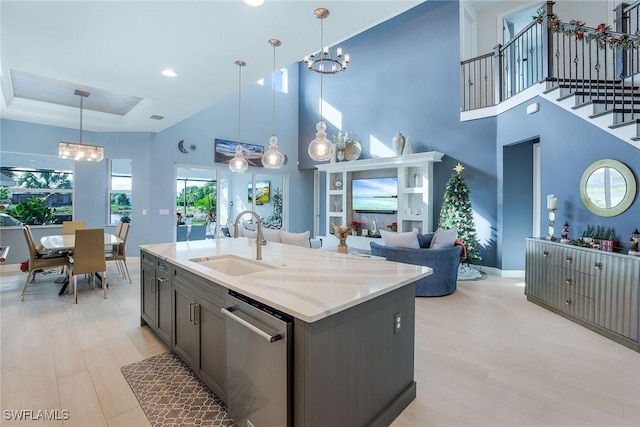 kitchen featuring sink, dishwasher, light hardwood / wood-style flooring, a towering ceiling, and pendant lighting