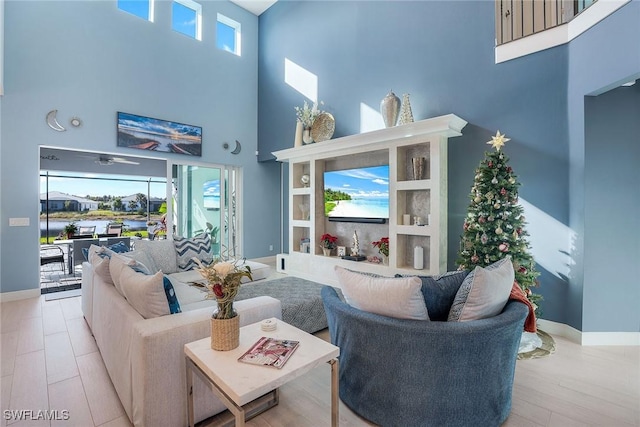 living room featuring ceiling fan, plenty of natural light, a towering ceiling, and light hardwood / wood-style flooring