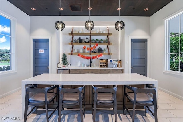 bar featuring light tile patterned floors, decorative light fixtures, stainless steel dishwasher, and sink