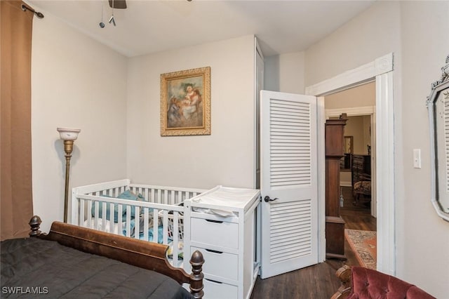 bedroom with ceiling fan, a crib, and dark wood-type flooring