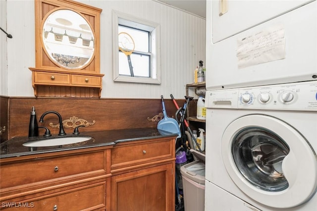 laundry room featuring cabinets, stacked washing maching and dryer, and sink