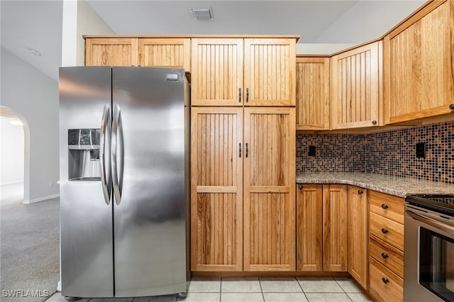 kitchen with decorative backsplash, appliances with stainless steel finishes, light stone counters, light tile patterned floors, and lofted ceiling