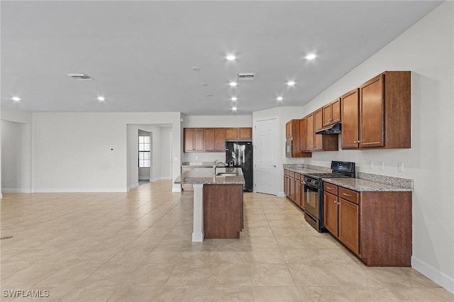 kitchen featuring sink, light stone counters, an island with sink, light tile patterned flooring, and black appliances