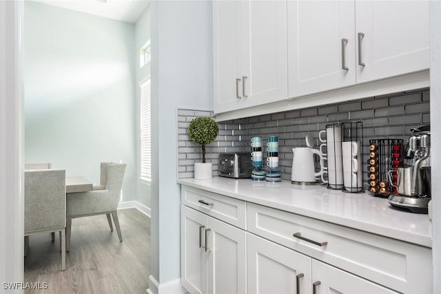 bar featuring backsplash, white cabinetry, and light hardwood / wood-style floors