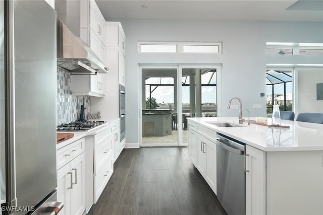 kitchen with white cabinets, a center island with sink, wall chimney range hood, sink, and appliances with stainless steel finishes