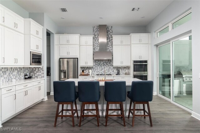 kitchen with decorative backsplash, appliances with stainless steel finishes, dark hardwood / wood-style flooring, wall chimney exhaust hood, and white cabinetry