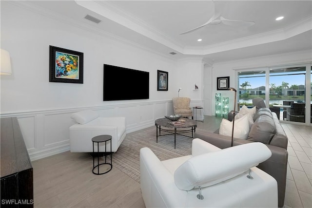 living room featuring ceiling fan, a raised ceiling, ornamental molding, and light hardwood / wood-style flooring