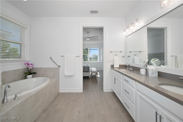 bathroom featuring hardwood / wood-style floors, vanity, and a relaxing tiled tub