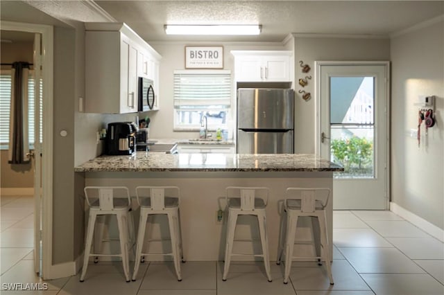 kitchen with appliances with stainless steel finishes, white cabinetry, plenty of natural light, and light stone counters