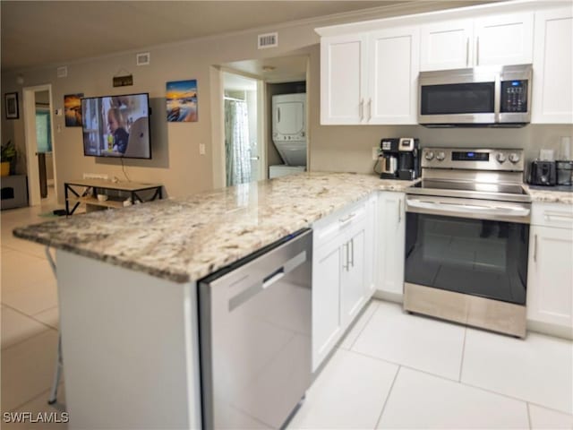 kitchen featuring kitchen peninsula, appliances with stainless steel finishes, light tile patterned flooring, white cabinetry, and stacked washer / dryer