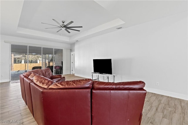 living room with ceiling fan, light wood-type flooring, and a tray ceiling