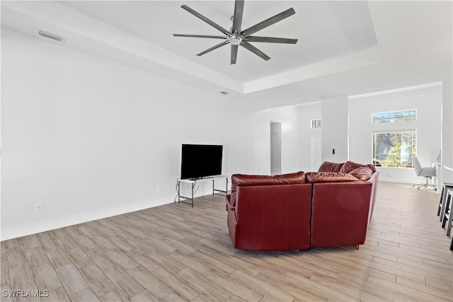 living room with a raised ceiling, ceiling fan, and light wood-type flooring