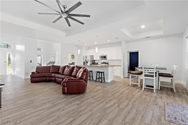 living room with a raised ceiling, ceiling fan, and light hardwood / wood-style floors