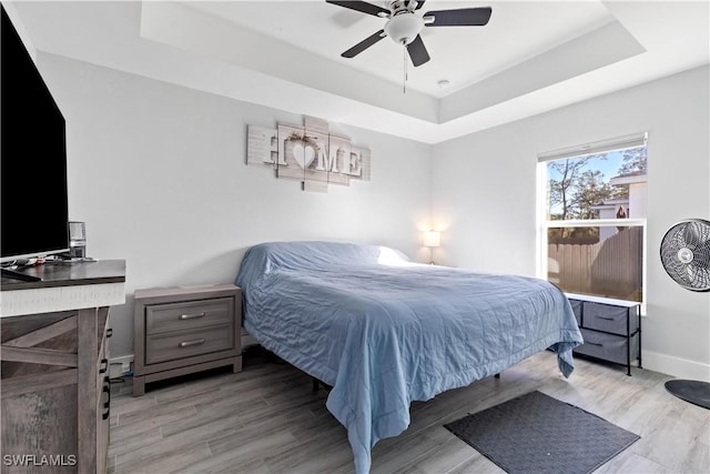 bedroom with a raised ceiling, ceiling fan, and light hardwood / wood-style flooring