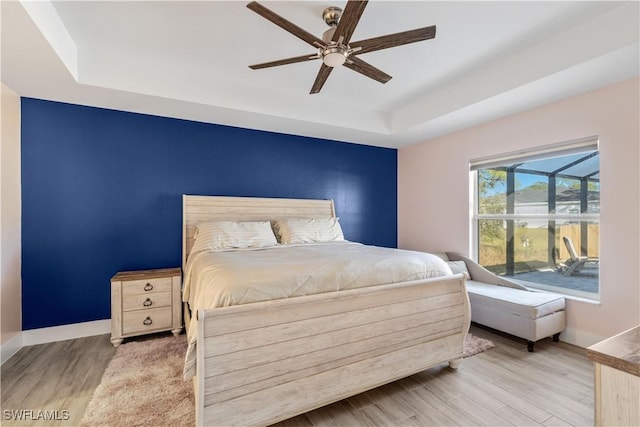 bedroom with a tray ceiling, ceiling fan, and light wood-type flooring