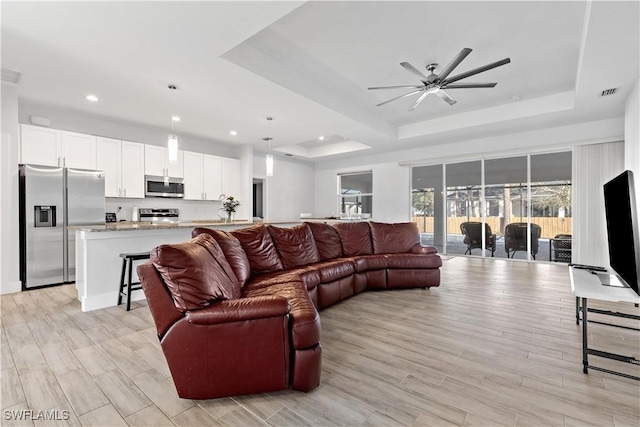 living room with a tray ceiling, ceiling fan, and light hardwood / wood-style floors